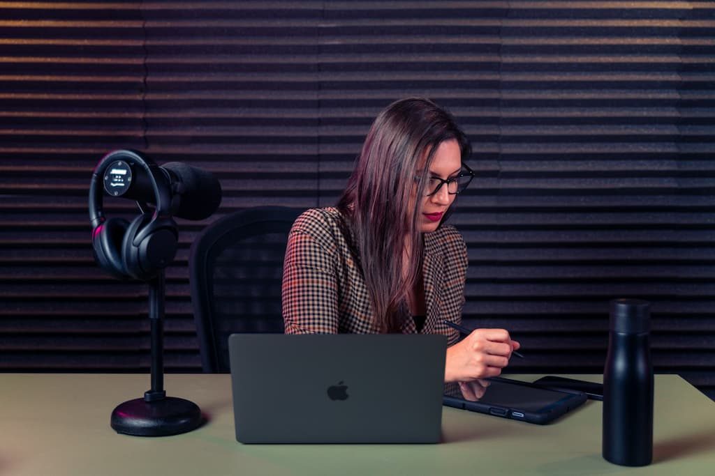 A woman working at a laptop beside a microphone in a dark studio