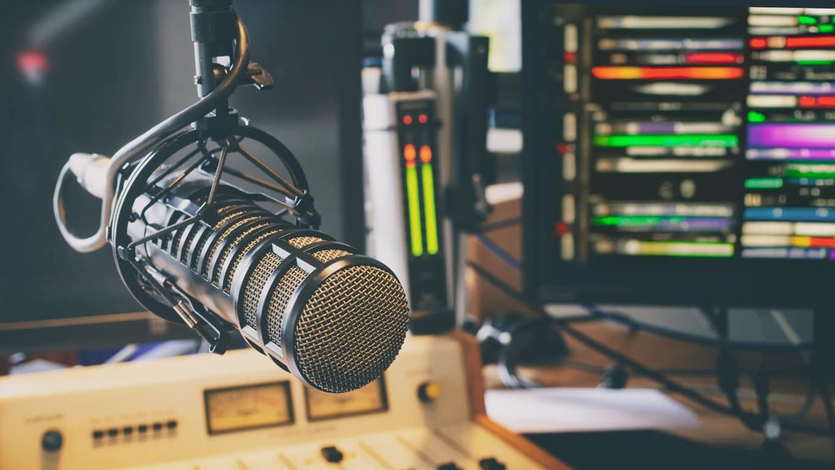 A silver microphone on a boom arm in front of a mixing desk