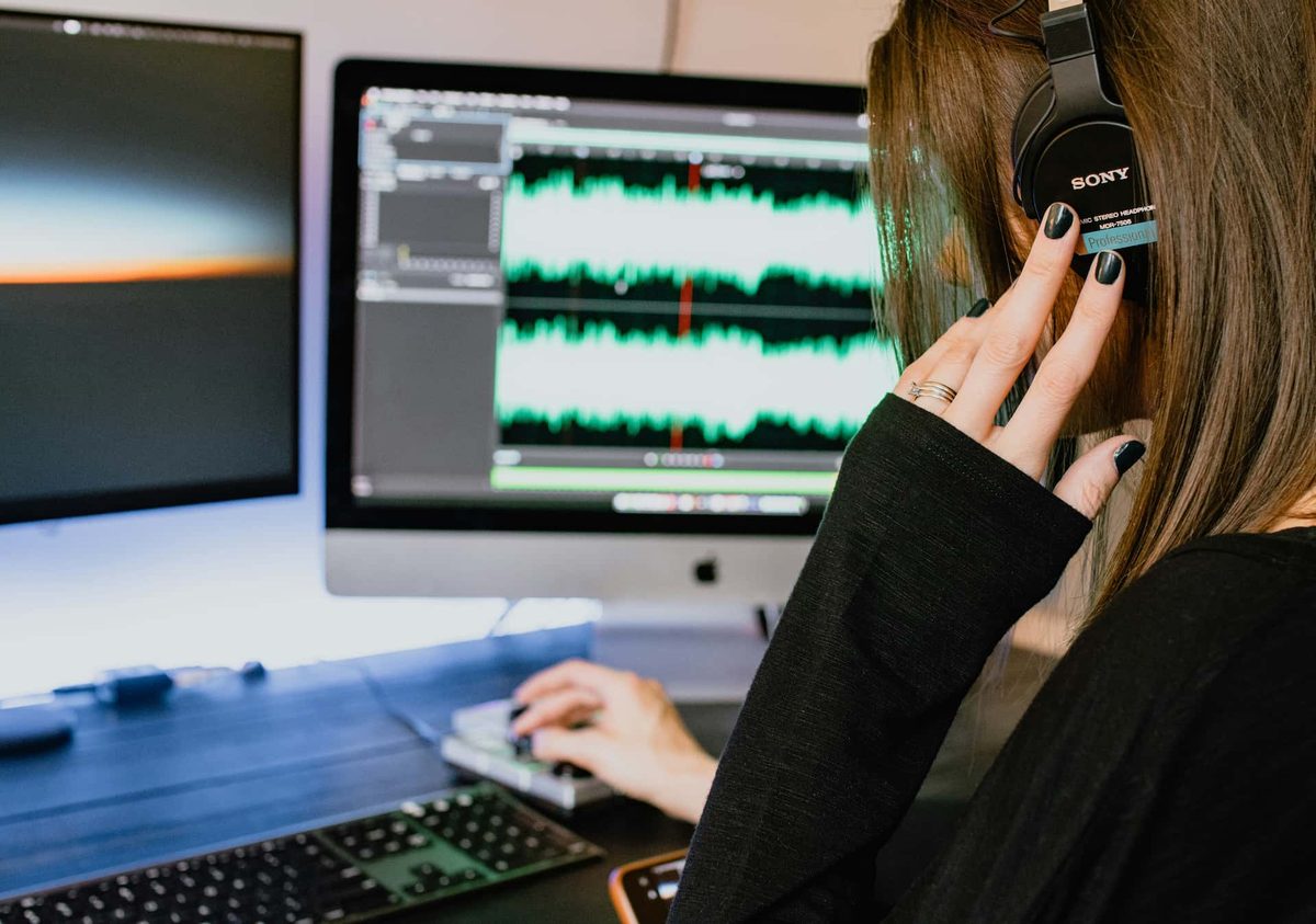 A person in headphones editing audio waveforms on a desktop computer