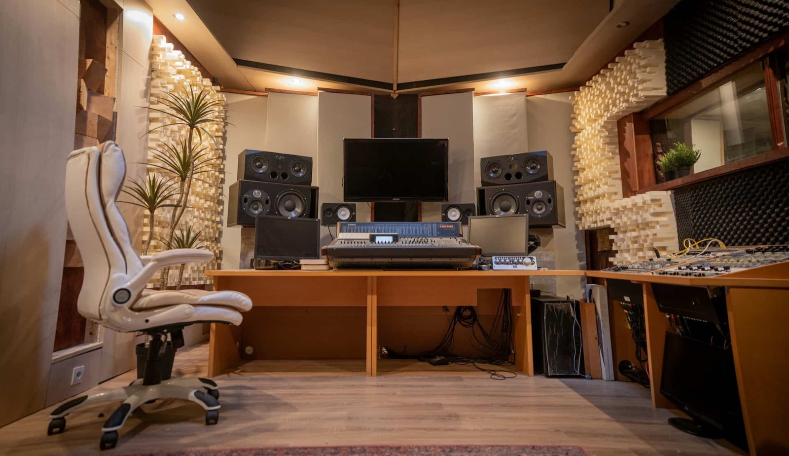 A control room with a mixing desk, monitor speakers, and wooden diffusers on the walls