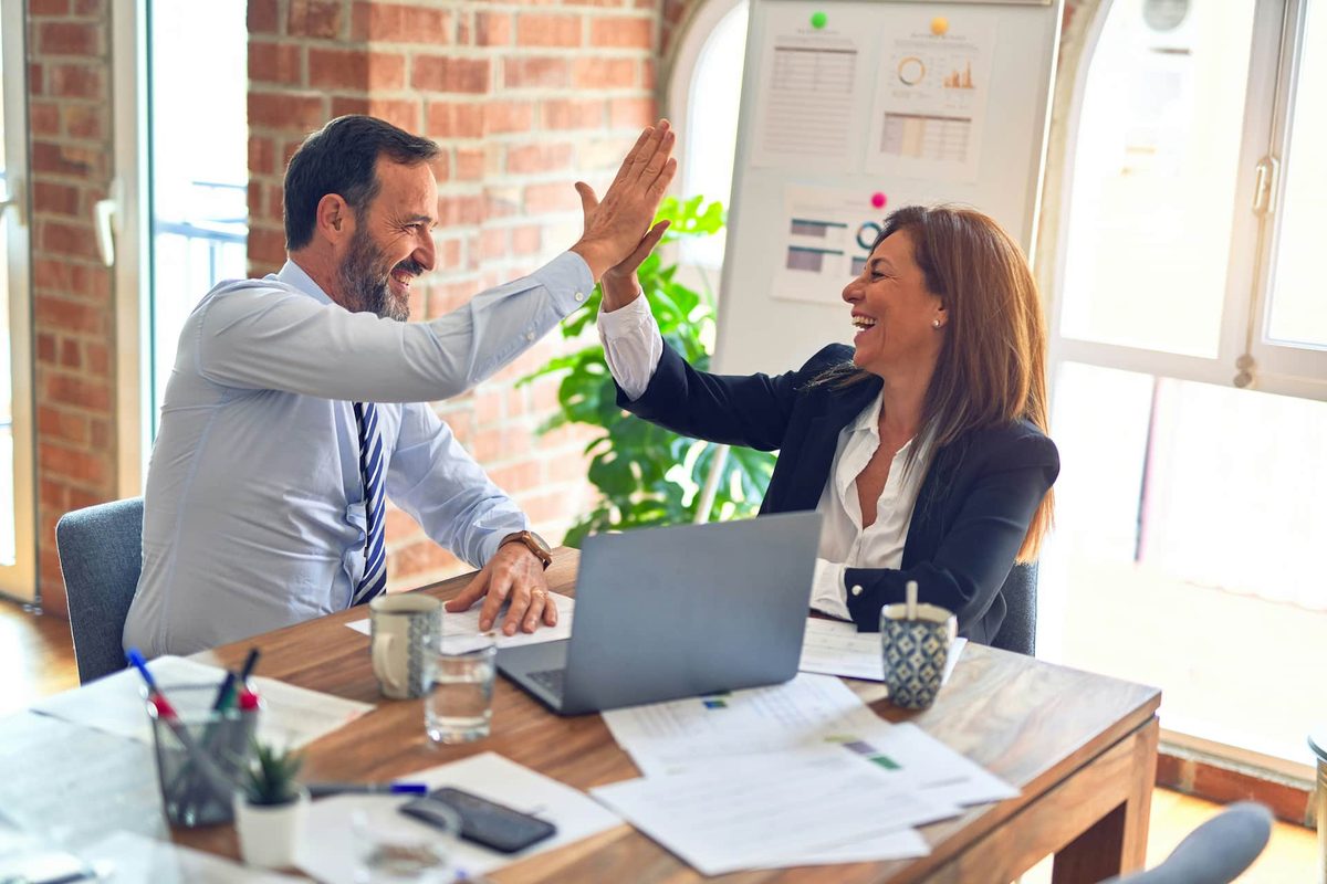 Two colleagues high-fiving across a desk of laptops and notebooks