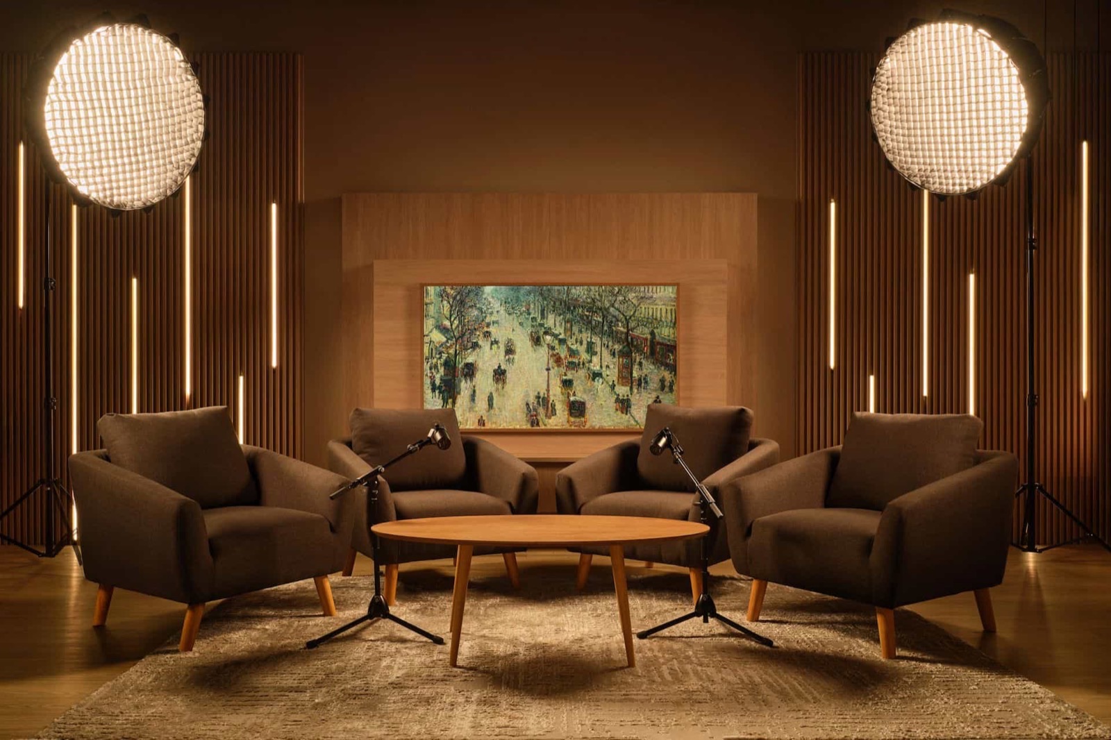 A warmly lit studio lounge: four armchairs around a low table, boom microphones, and softboxes against slatted wood walls