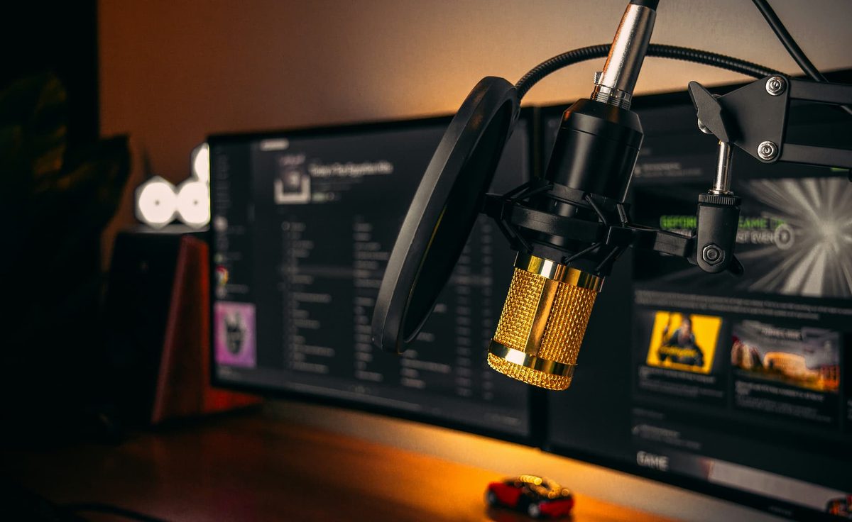 A gold condenser microphone in front of a monitor in a warmly lit studio