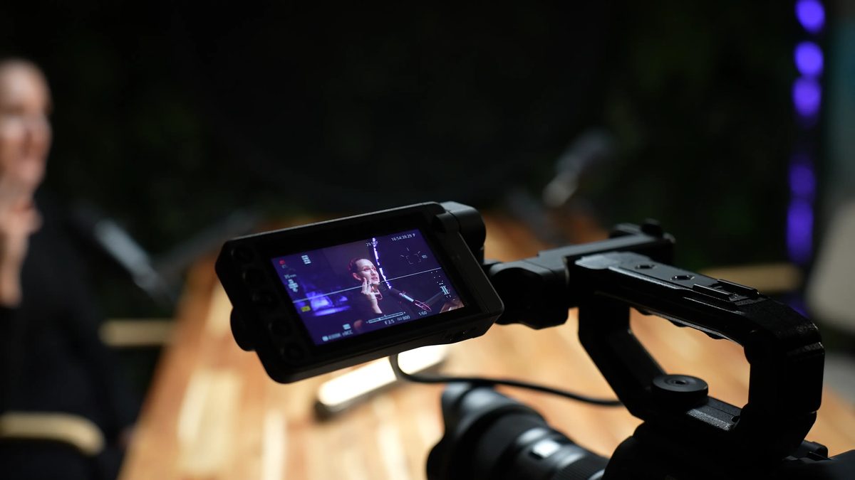 A camera monitor showing a host being filmed in a studio