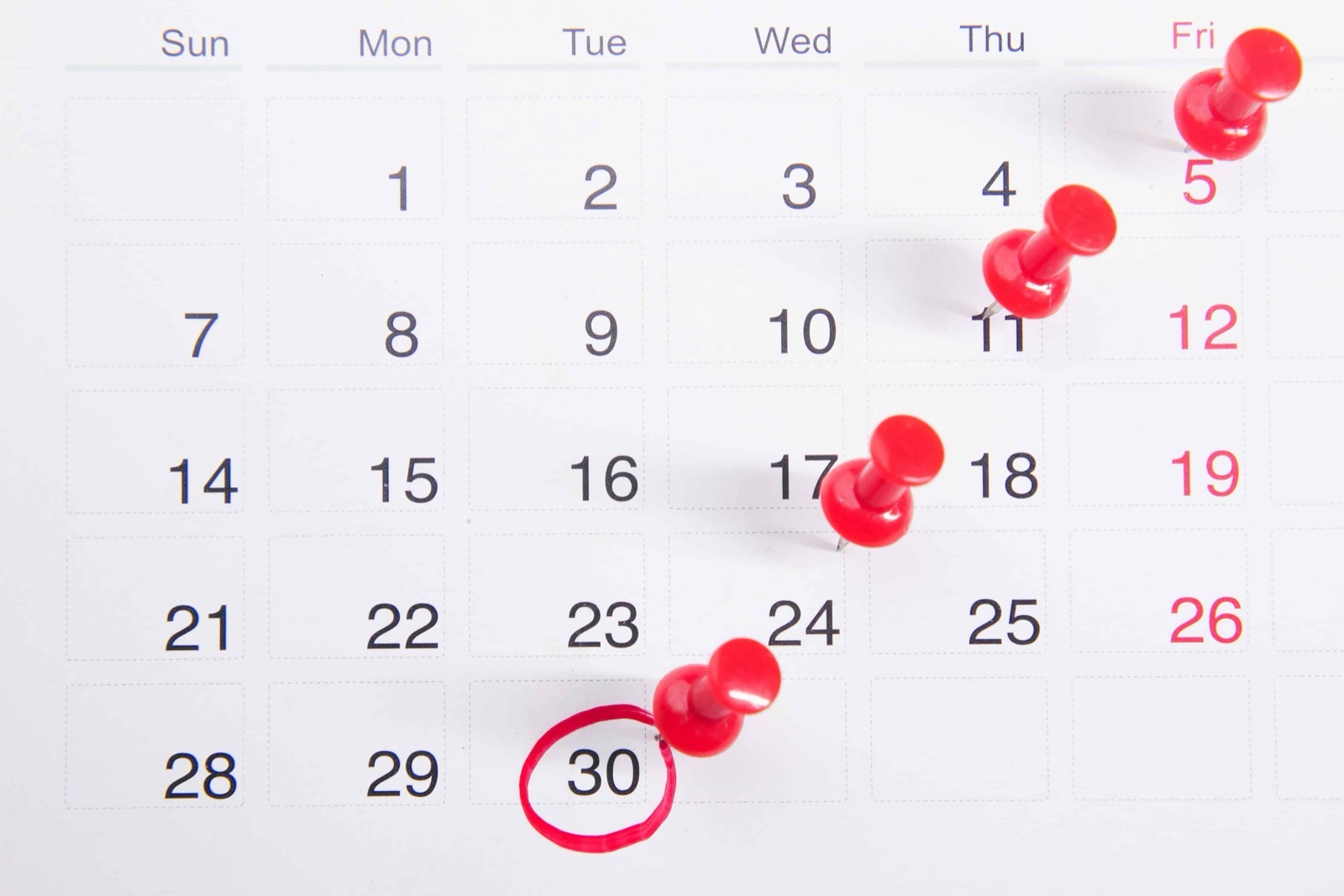 A wall calendar with red pins and the 30th circled