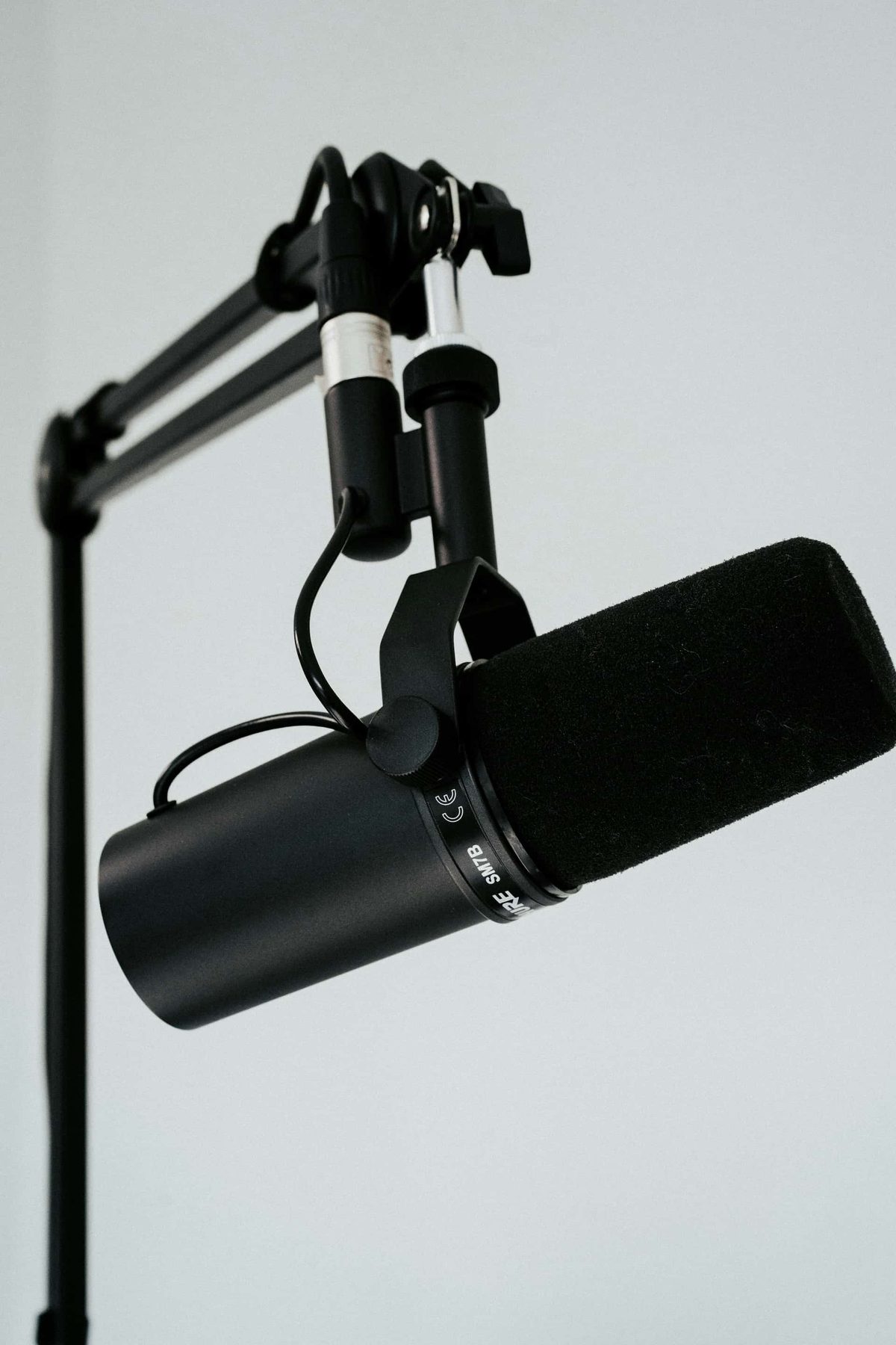 A broadcast microphone on a boom arm against a plain background
