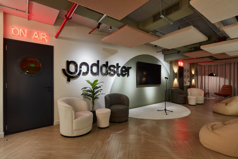 A studio reception with the Poddster logo, an on-air sign, and soft seating