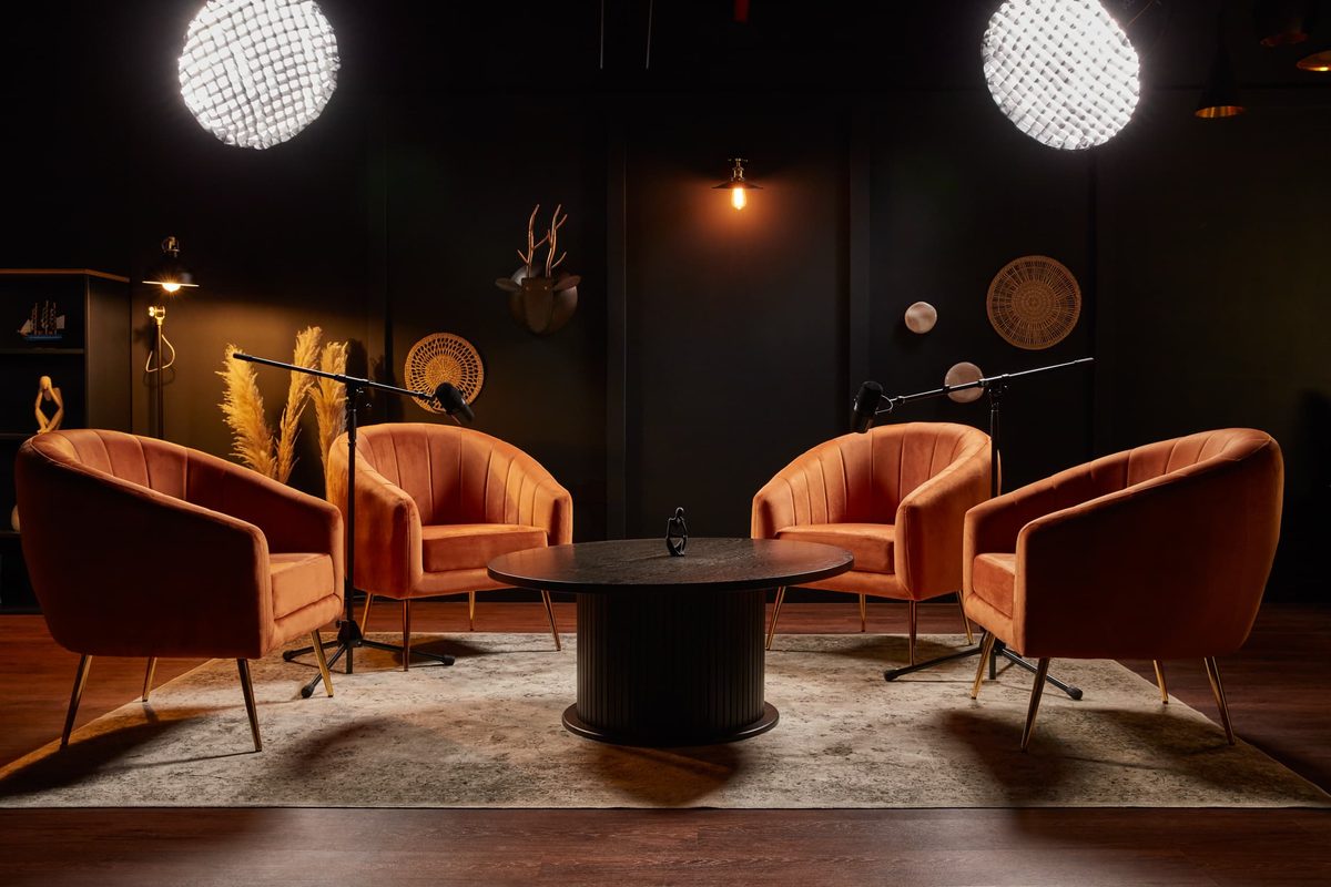Four orange armchairs around a low table in a dark studio