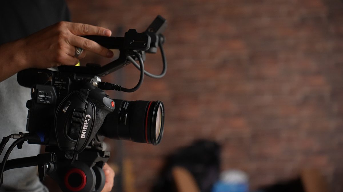 A camera operator filming against a brick wall