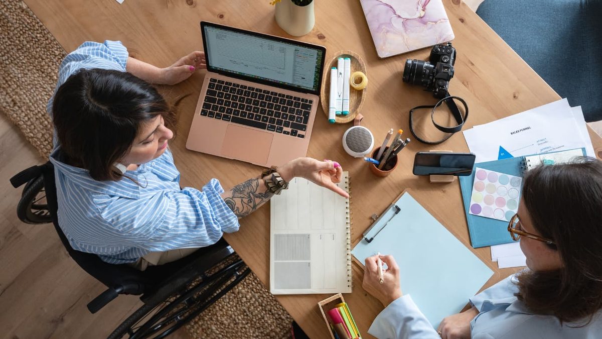 Two people working over laptops and notebooks at a desk, seen from above