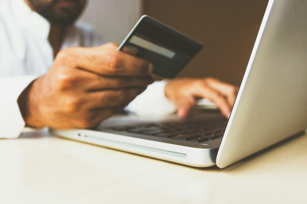 A person holding a bank card while typing on a laptop