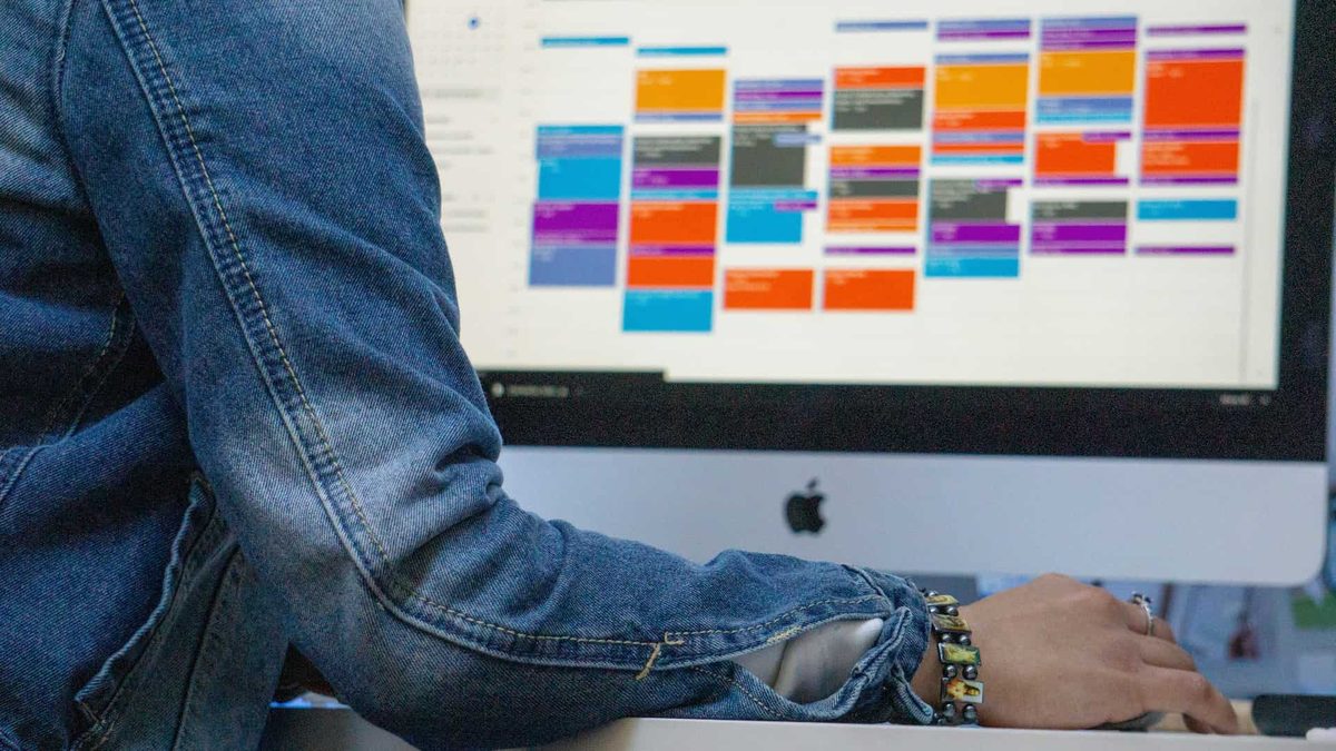 A person working at an iMac showing a colourful project board