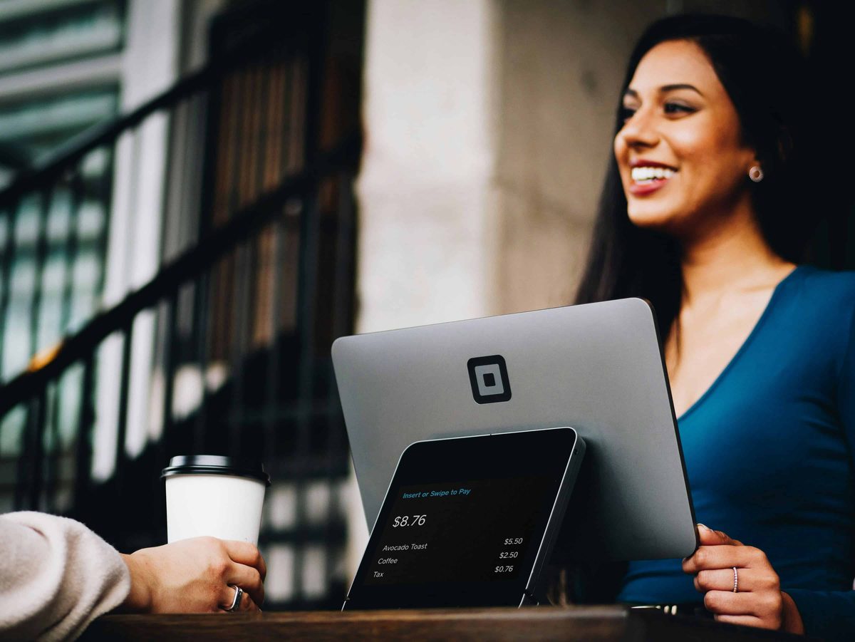 A woman smiling as she takes a card payment on a tablet