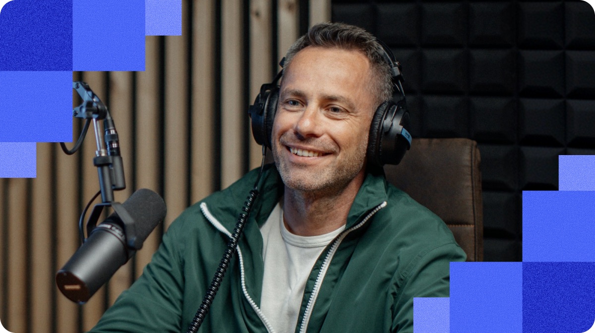 A host smiling behind a microphone in an acoustically treated studio, framed by blue tiles