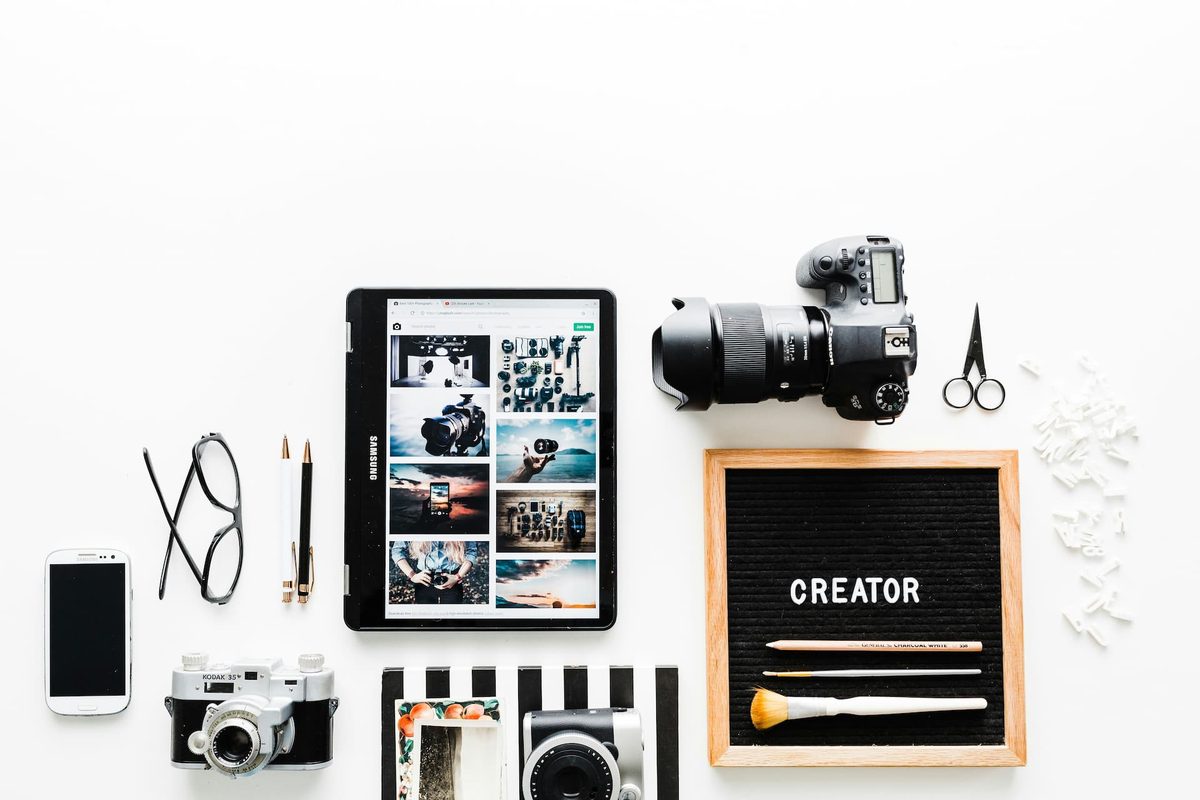 A flat lay of a camera, tablet, and phone beside a letter board reading: creator